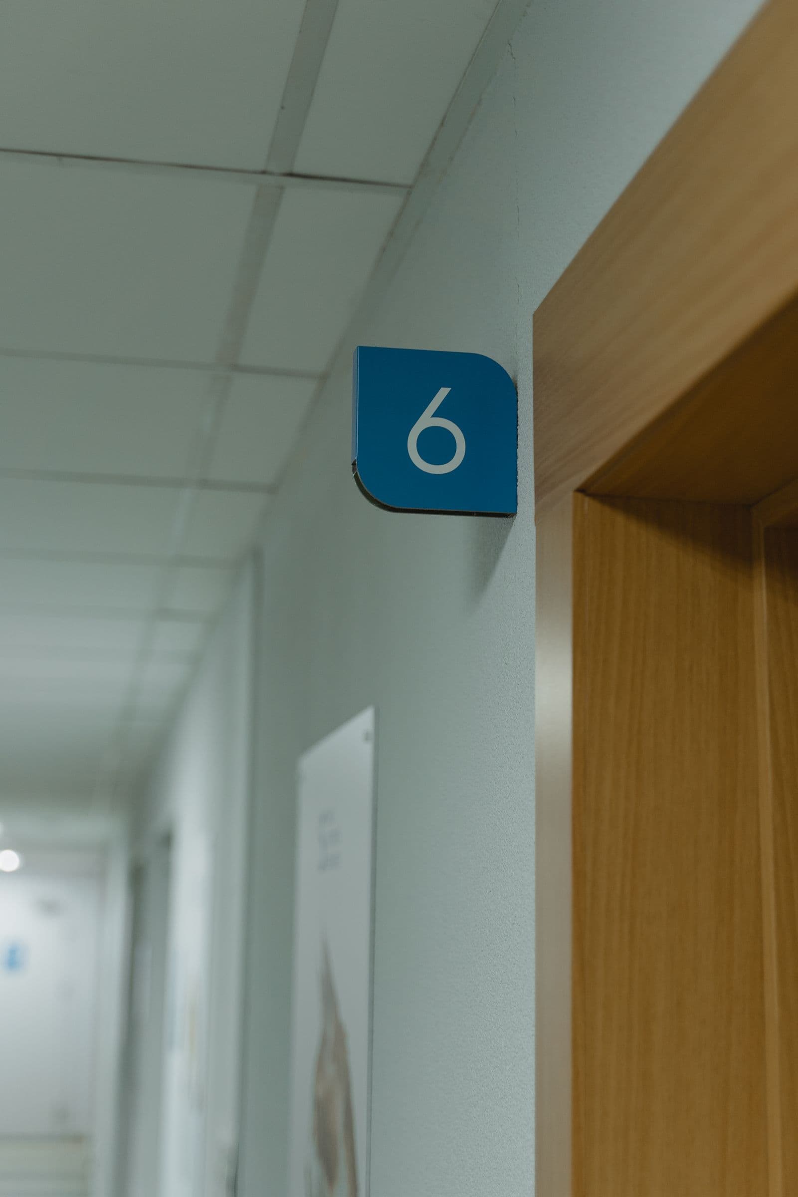 Blue room number sign mounted on a wall in a commercial medical facility corridor