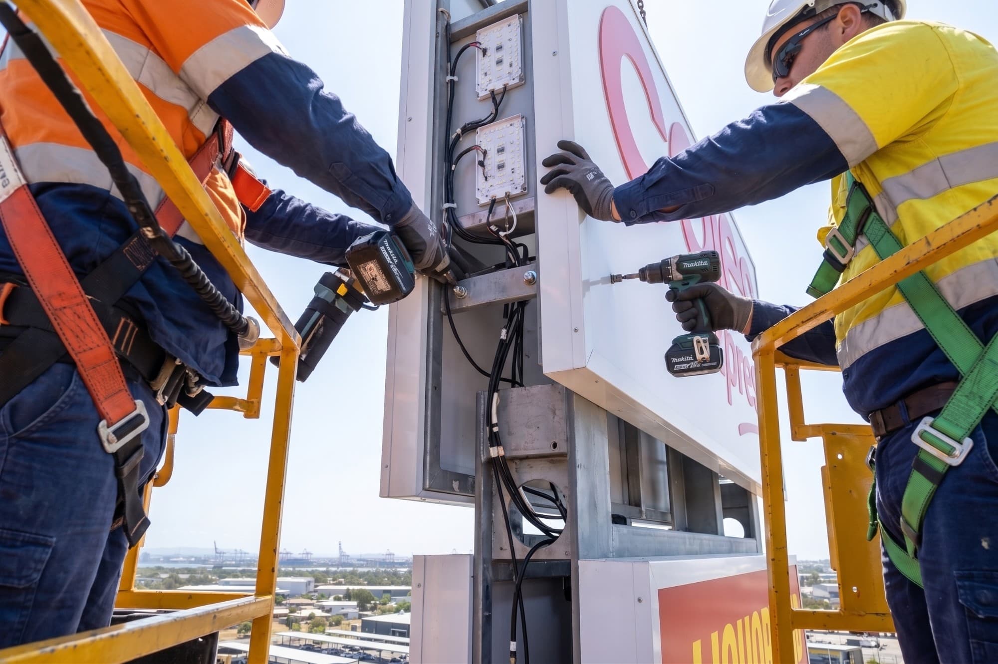 Installers wiring LED illumination modules inside an elevated pylon sign cabinet